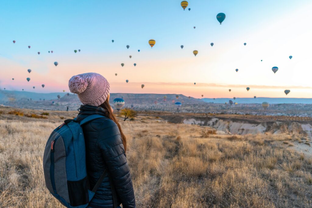 Woman watching hot air balloons in Cappadocia at sunrise, a popular travel destination.